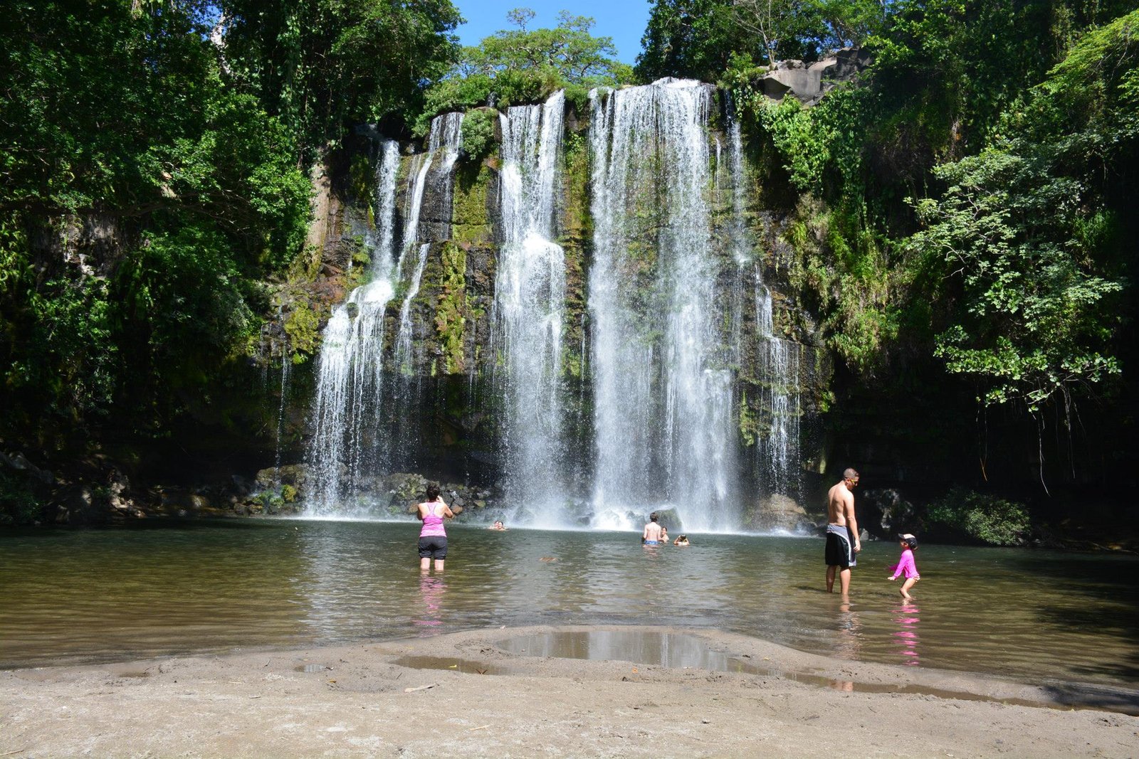 "Scenic view of Miravalles Waterfalls surrounded by lush green forest, with crystal-clear water cascading down rocky cliffs into a serene pool below."